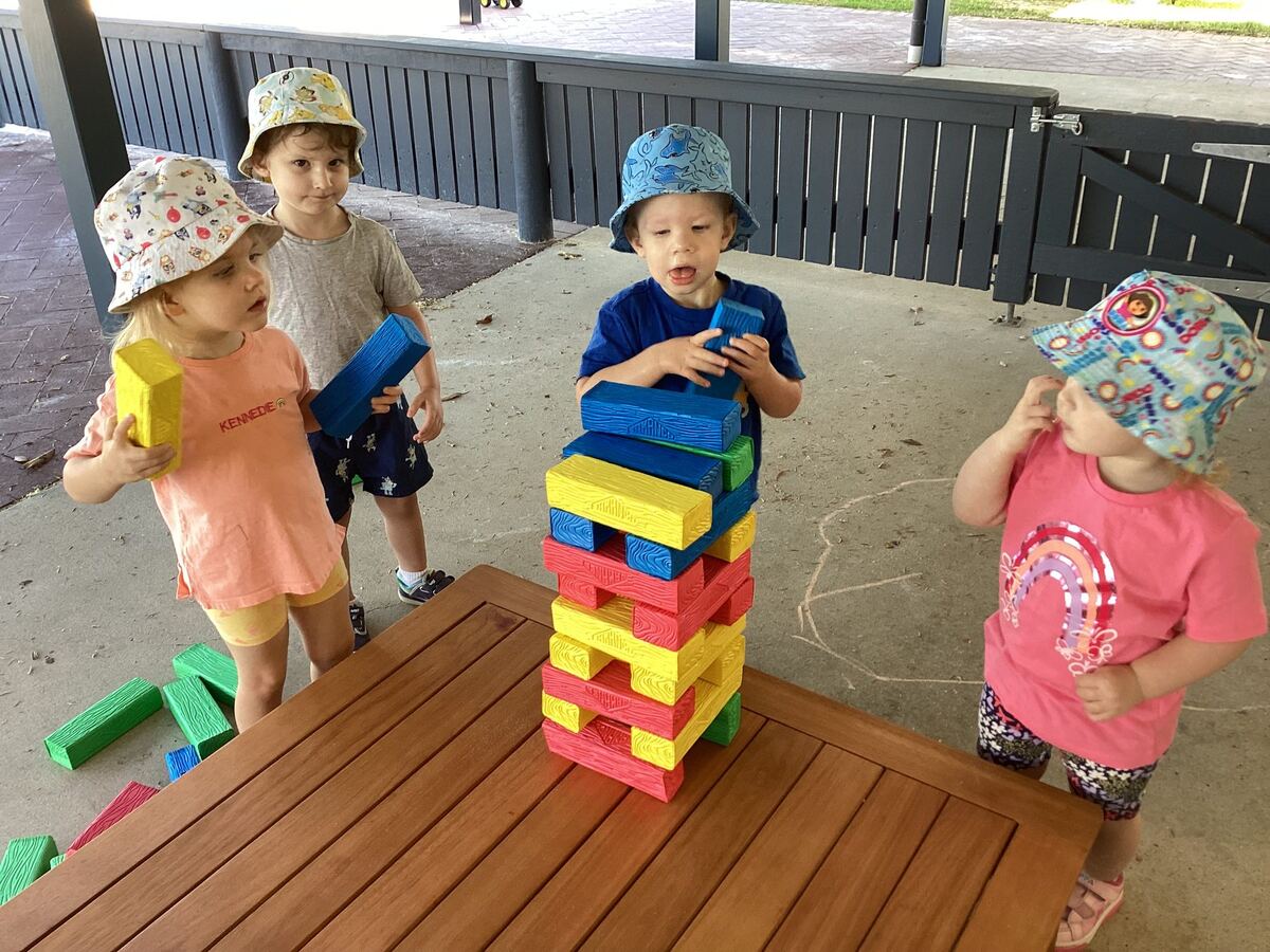 Four young children build a tall tower of coloured blocks outdoors