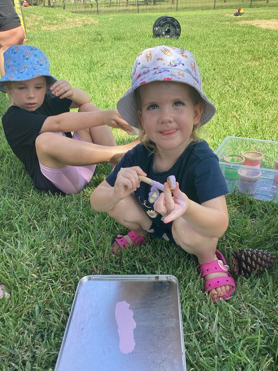 Two children work with clay on a tray outdoors