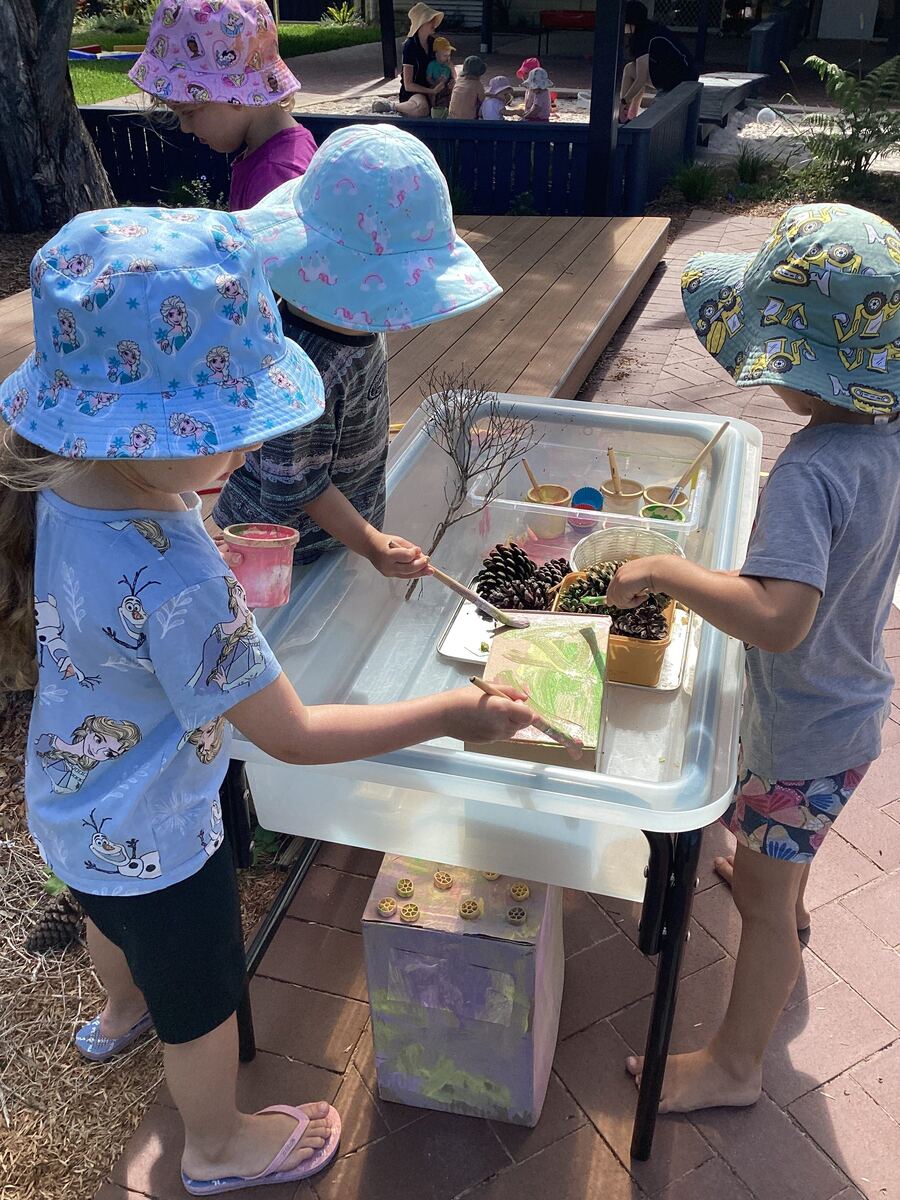 Children at a water table outdoors, mixing paint with pine cones