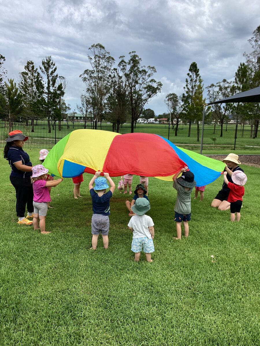 Children and educators play with a colourful parachute on the grass
